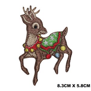 Może przedstawiać: Haftowany naszywka do prasowania z brązowym reniferem z czerwoną, zieloną i białą girlandą wokół szyi. Renifer ma 8,3 cm x 5,8 cm.