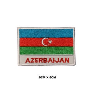 May include: Embroidered patch featuring the flag of Azerbaijan. The patch is white with a blue, red, and green flag in the center. The flag has a white crescent moon and star. The words "AZERBAIJAN" are written in white below the flag. The patch measures 9 cm by 6 cm.
