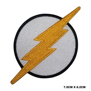 May include: A white and gold embroidered patch featuring the Flash logo. The logo is a lightning bolt inside a circle with a black outline. The patch measures 7.5 cm by 6.2 cm.