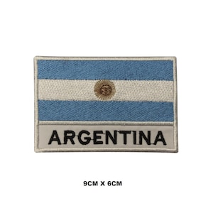May include: An embroidered patch featuring the Argentinian flag with the words "ARGENTINA" below. The flag is blue and white with a yellow sun in the center. The patch is 9 cm by 6 cm.