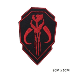 May include: Red and black embroidered patch featuring the Mandalorian symbol, a skull with horns, on a black background. The patch is 9 cm by 6 cm.