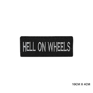 May include: A black rectangular patch with white embroidered text reading "HELL ON WHEELS". The patch is 10cm x 4cm.
