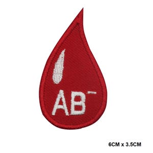 Puede incluir: Parche rojo en forma de gota de sangre con el texto "AB-" bordado en blanco y una gota blanca más pequeña en su interior. El parche mide 6 cm por 3,5 cm.