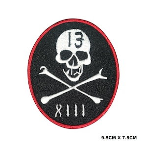 May include: Black and red embroidered patch with a white skull and crossbones. The skull has the number "13" on its forehead and the number "XIII" below the crossbones. The patch measures 9.5 cm by 7.5 cm.