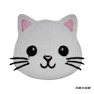 Könnte beinhalten: Gestickter Aufnäher in Form eines Katzenkopfes. Die weiße Katze hat schwarze Augen, Schnurrhaare und eine Nase, mit rosa Innenohren. Der Aufnäher misst 7 cm x 6 cm.