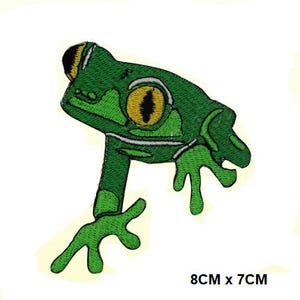 May include: Embroidered green frog patch with yellow and black eye details. The patch measures 8cm by 7cm. The frog is depicted in a side profile with its legs extended. The patch is suitable for clothing or accessories.