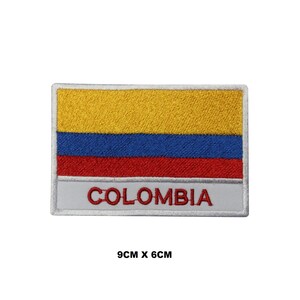 May include: An embroidered patch featuring the Colombian flag with yellow, blue, and red stripes. The patch is white with a white border and the word "COLOMBIA" in red lettering. The patch measures 9 cm by 6 cm.