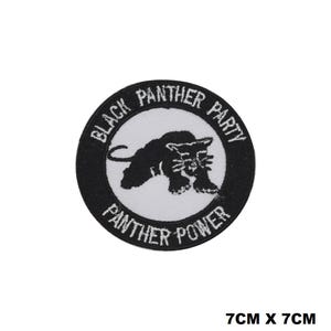 Pode incluir: Etiqueta bordada em preto e branco com uma silhueta de pantera negra e o texto "Black Panther Party" e "Panther Power". A etiqueta mede 7 cm por 7 cm.