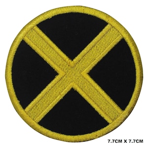 Op de afbeelding: Een zwarte ronde patch met een geborduurd X-vormig ontwerp in geel. De patch heeft een diameter van 7,7 cm.