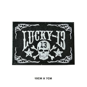 May include: Black and white embroidered patch with a skull and crossbones, the text "LUCKY-13" and a spiderweb design. The patch measures 10 cm by 7 cm.