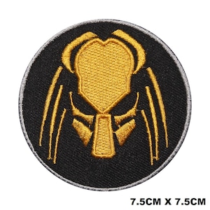 Op de afbeelding: Een geborduurde patch in zwart en goud met het iconische masker van de Predator. De patch is rond en heeft een diameter van 7,5 cm.