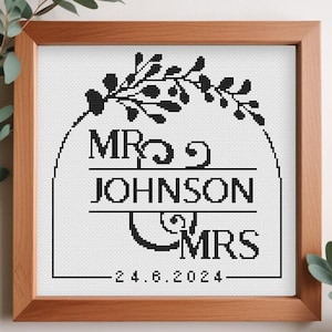 May include: Black and white cross-stitch design with a floral wreath, the text "Mr. & Mrs. Johnson" and the date "24.6.2024".