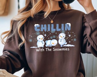 May include: A brown sweatshirt with the text "CHILLIN With The Snowmies" in blue. The graphic features three snowmen, snowflakes, and snow. The sweatshirt is a crew neck style.