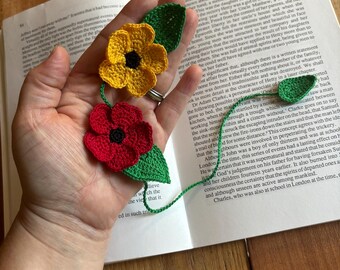 Puede incluir: Un marcapáginas de ganchillo con flores rojas, amarillas y verdes. El marcapáginas está hecho de hilo y es una artesanía hecha a mano.
