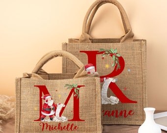 May include: Two burlap tote bags with handles. The bags feature a large red letter, a Santa Claus graphic, and the name "Michelle" and "Rianne". The bags are decorated with Christmas-themed elements.