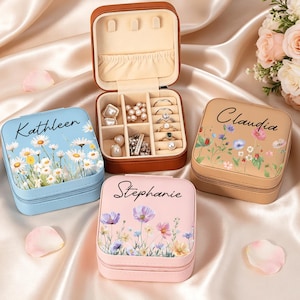 以下が含まれることがあります： ファスナー付きの正方形のジュエリーボックス3点。花柄がプリントされ、Kathleen、Stephanie、Claudiaの名前が入っています。1つは開いた状態で、リング、イヤリング、ネックレス用の仕切りがあるクリーム色の内部が見えています。