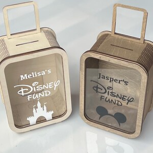 K&ouml;nnte beinhalten: Zwei Holzspardosen in Form von Koffern. Eine Box hat "Melisa's Disney Fund" und eine Burg, die andere "Jasper's Disney Fund" und einen Mickey Mouse Kopf. Beide haben einen Schlitz f&uuml;r Geld und einen Griff.