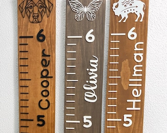 May include: Three wooden growth charts featuring geometric animal and insect cutouts. The first shows a dog and the name Cooper, the second a butterfly and Olivia, and the third a bison and Hellman. Each board displays height markings from 5 to 6.