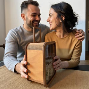 K&ouml;nnte beinhalten: Ein Paar l&auml;chelt, w&auml;hrend es auf eine Holzkiste mit einer Glasfront schaut. Die Kiste hat einen Griff und ist mit kleinen Gegenst&auml;nden gef&uuml;llt. Die Kiste ist ein einzigartiges und durchdachtes Geschenk.
