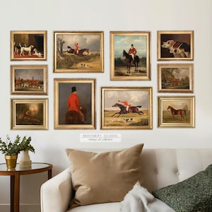 May include: A gallery wall featuring nine framed paintings depicting scenes of fox hunting with horses and riders in red coats. The paintings are set against a white wall with a couch and side table in the foreground.