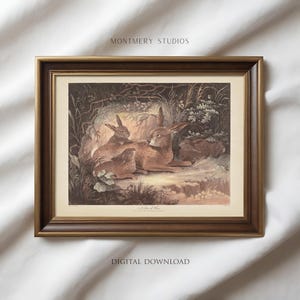 Puede incluir: Una impresión enmarcada con una ilustración vintage de liebres marrones en un entorno natural. La obra de arte está enmarcada en un marco de madera marrón oscuro. El texto "MONTEMRY STUDIOS" y "DIGITAL DOWNLOAD" son visibles.