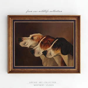 Pode incluir: Uma pintura a óleo vintage de três cães de caça com pelagem marrom, branca e preta. Os cães estão olhando para a esquerda do quadro. A pintura é emoldurada em uma moldura dourada com um passe-partout azul escuro.