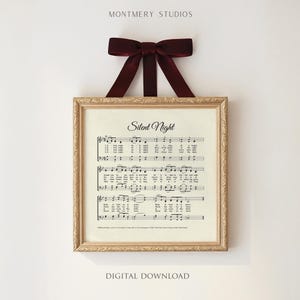 May include: A framed print of the "Silent Night" musical score, featuring a gold-colored ornate frame and a burgundy velvet bow at the top. The text "Silent Night" is displayed in elegant script above the musical notes. The words "Digital Download" are at the bottom.