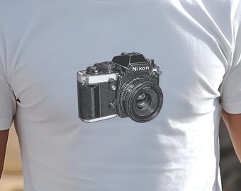 以下が含まれることがあります： ニコンカメラの白黒イラストが描かれた白いTシャツです。