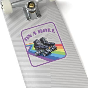 May include: A sticker with a pair of black roller skates with white laces and silver wheels, set against a rainbow gradient. The text "ON A ROLL" is in purple, within a purple rectangular border.