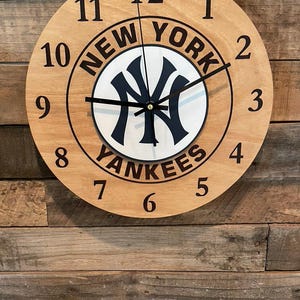 May include: A wooden clock with a New York Yankees logo and the words "New York Yankees" around the edge. The clock face is white with black hands and black numbers.