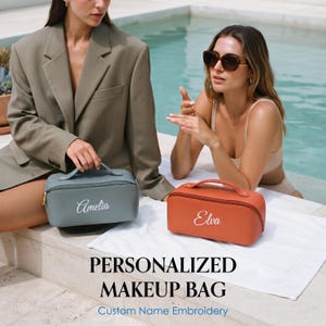 May include: Two rectangular makeup bags with top handles and gold zippers. One bag is sage green with the name Amelia embroidered in white, and the other is terracotta orange with the name Elva embroidered in white. Text reads: PERSONALIZED MAKEUP BAG.