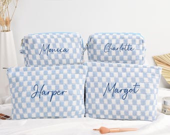 May include: Four rectangular zippered pouches featuring a light blue and white checkered pattern. Each pouch is personalized with dark blue cursive embroidery displaying the names Monica, Charlotte, Harper, and Margot on the front center.