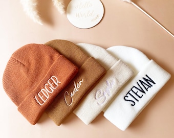 May include: Four knitted beanies in different colors with embroidered names: Ledger, Caden, Sylvie, and Stevan.