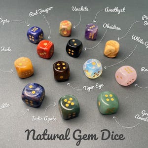May include: A collection of twelve multi-colored natural gemstone dice labeled as Lapis, Red Jasper, Unakite, Amethyst, Obsidian, Picture Stone, Yellow Jade, Tiger Eye, White Opal, Rose Quartz, Sodalite, India Agate, and Green Aventurine.