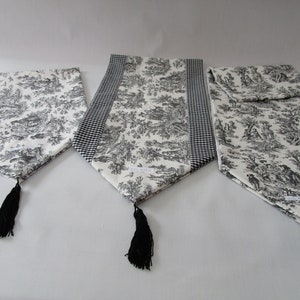 May include: Three black and white table runners with black tassels. The runners have a toile pattern and one has a black and white gingham border.
