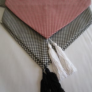 May include: A red and white gingham table runner with black and white gingham trim and white tassels.