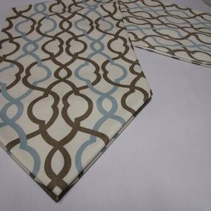 May include: A white table runner with a geometric pattern in brown and blue. The pattern is a repeating design of interlocking circles and lines.