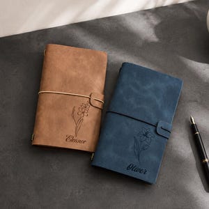 Könnte beinhalten: Zwei rechteckige Notizbücher mit Gummibandverschluss, eines in Hellbraun und eines in Blau. Das hellbraune Notizbuch zeigt eine Blumen-Strichzeichnung und den Namen Eleanor. Das blaue Notizbuch zeigt eine Blumen-Strichzeichnung und den Namen Oliver.