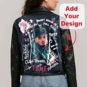 Könnte beinhalten: Schwarze Lederjacke mit individuellem Design auf dem Rücken. Das Design zeigt ein Porträt von Chris Brown, Graffiti-Text und rote Farbspritzer. Die Jacke wird von einer Person in blauen Jeans getragen.