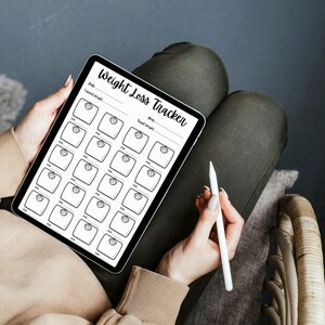 May include: A black and white weight loss tracker on a tablet with a white stylus. The tracker has a section for dates and a section for weight with a scale icon for each day.
