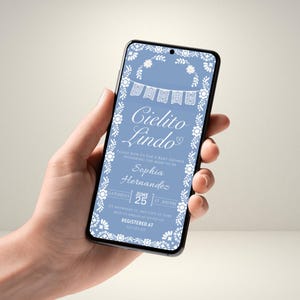 May include: A smartphone displays a baby shower invitation. The invitation features the words "Cielito Lindo" in elegant script, surrounded by floral and banner designs. The invitation is in a light blue colour with white accents. The date and time are also displayed.