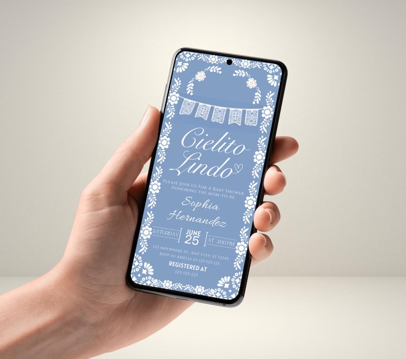 May include: A smartphone displays a baby shower invitation. The invitation features the words "Cielito Lindo" in elegant script, surrounded by floral and banner designs. The invitation is in a light blue colour with white accents. The date and time are also displayed.