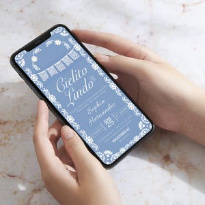 May include: A light blue baby shower invitation displayed on a smartphone. The invitation features white floral and banner designs, with the words "Cielito Lindo" in elegant script. Details include the name Sophia Hernandez, date, and time.