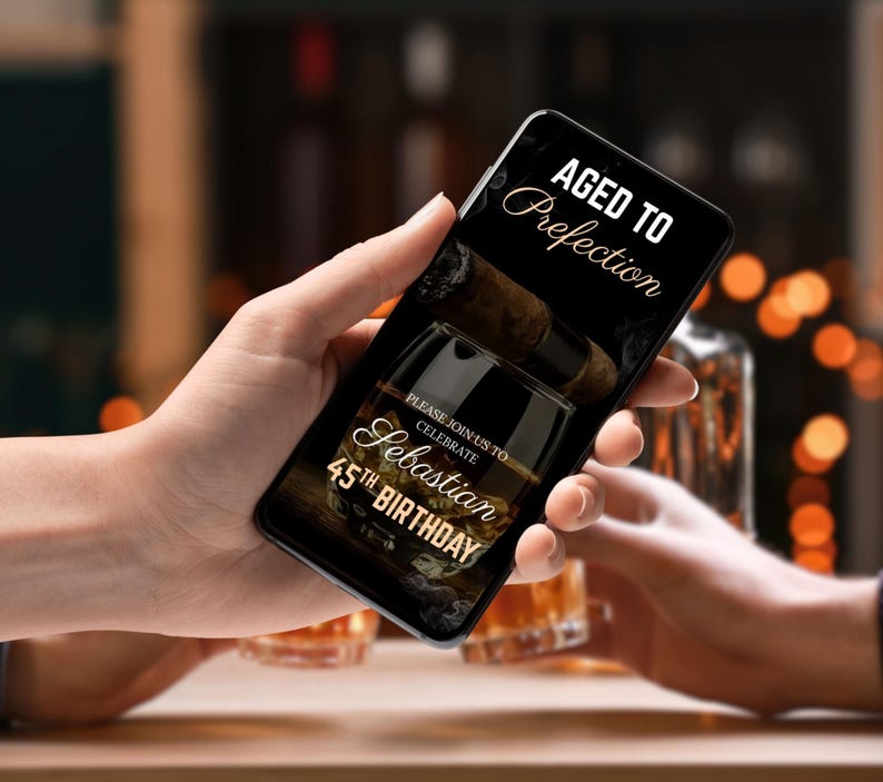 May include: A smartphone displaying a birthday invitation with a black background and gold text. The invitation reads "Aged to Perfection" and "Please join us to celebrate Sebastian's 45th Birthday". The image also features a glass of whisky and a cigar.