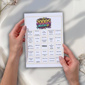 May include: A white bingo card with a gold border is held by two hands. The card is titled "2000s Music Bingo" and features a grid of song titles. The word "FREE" is in the center of the card.