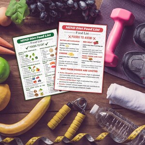 May include: Two MIND Diet Food List printable guides with a checklist of foods to eat and foods to avoid. The guides are on a wooden table with a measuring tape, a water bottle, hand weights, a towel, and a pair of sneakers.