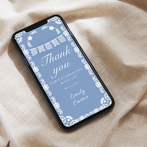 May include: A smartphone screen shows a digital invitation with a pale blue backdrop. The design includes white floral and banner motifs, with the words "Thank you" in a graceful script. The text "For celebrating with us! With love, Emily Carter" is also present.
