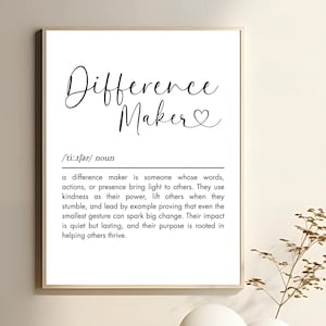 May include: A framed print with the words "Difference Maker" in elegant script, with a heart symbol. Below, a definition of "difference maker" is printed in a clear, easy-to-read font. The print is in a neutral color palette.