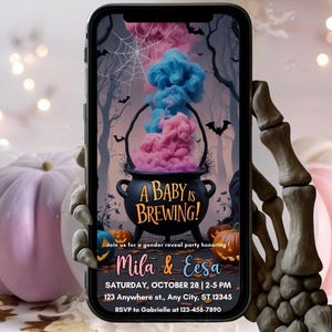 May include: A smartphone displays a Halloween-themed gender reveal party invitation. The design features a black cauldron with pink and blue smoke, bats, and pumpkins. Text reads "A Baby is Brewing!" and includes party details.