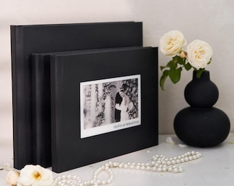 May include: Black leather photo album with a black and white photo of a couple in a garden. The album has a white border around the photo and the text "Olivia & Sebastian" printed below the photo.